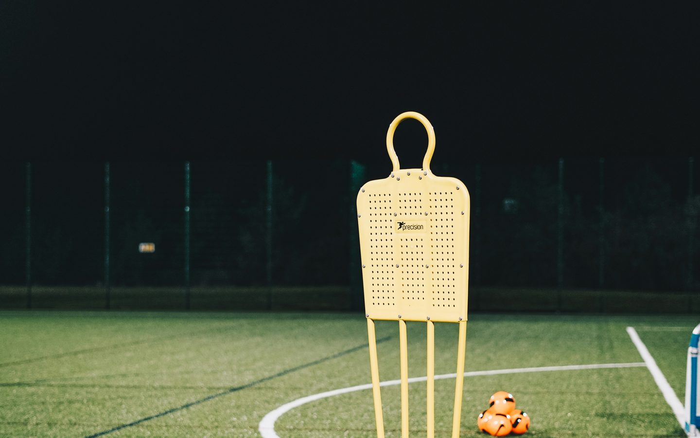 Un mannequin d’entraînement et des plots sur un terrain éclairé de nuit.